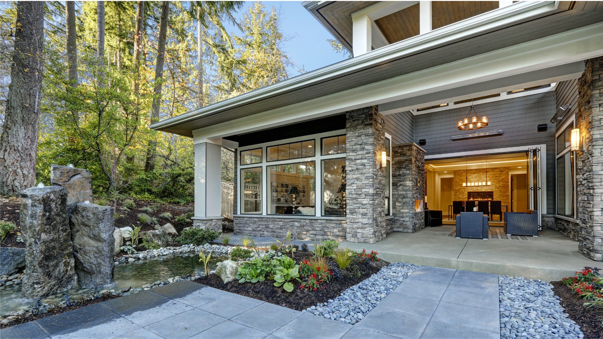 Custom craftsman home with stone columns, covered outdoor living area, and landscaped water feature